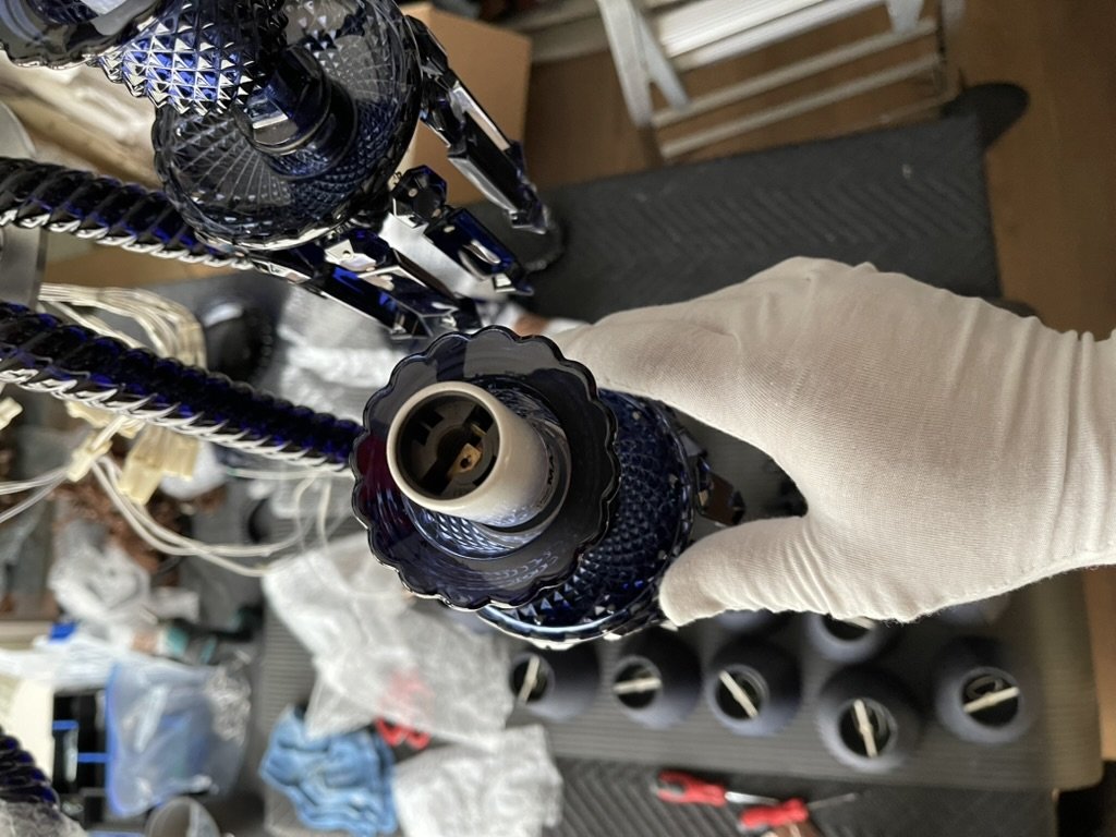 A white-gloved Brightmen technician handling a cobalt crystal chandelier arm